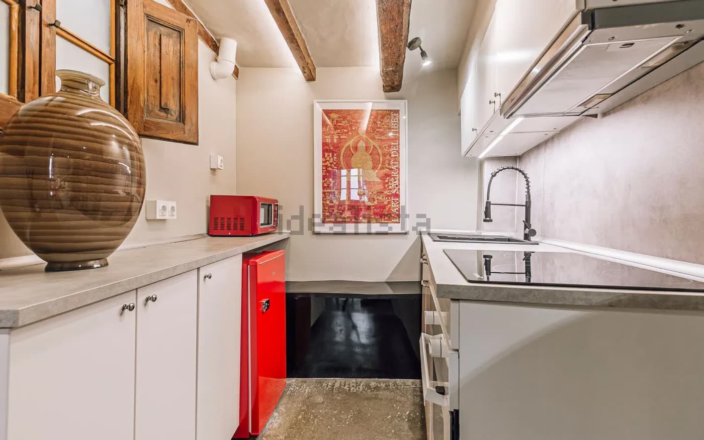 Cocina con encimera clara, nevera roja y una gran tinaja de cerámica