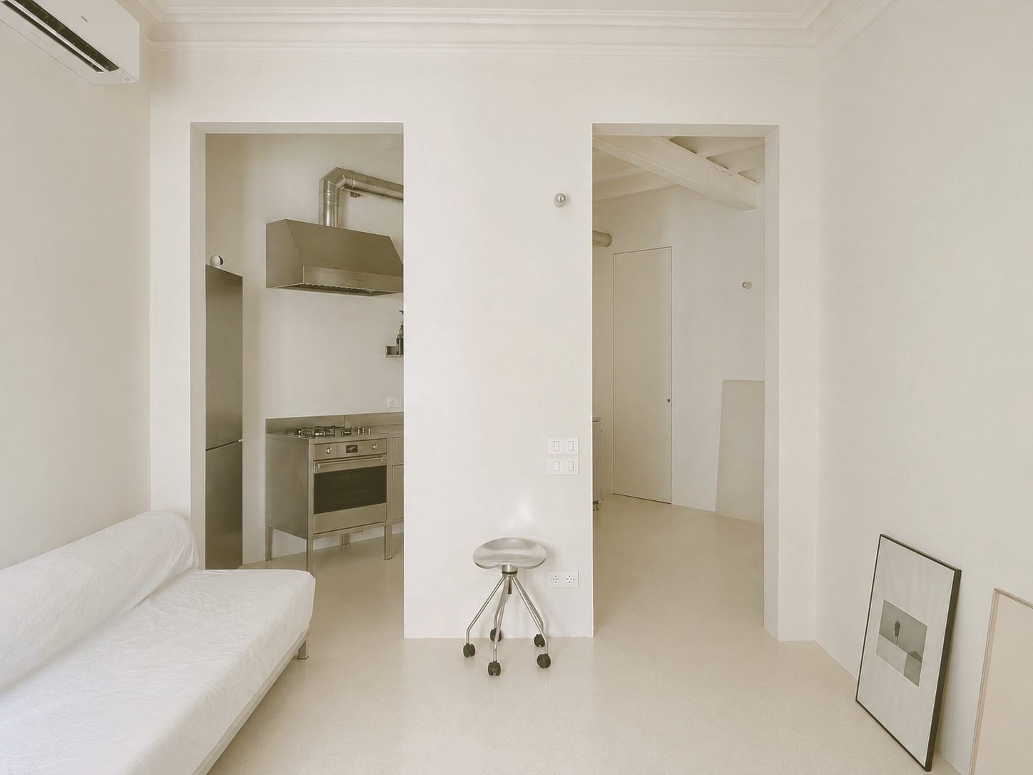 Salón con banco corrido blanco y la cocina semiabierta al fondo