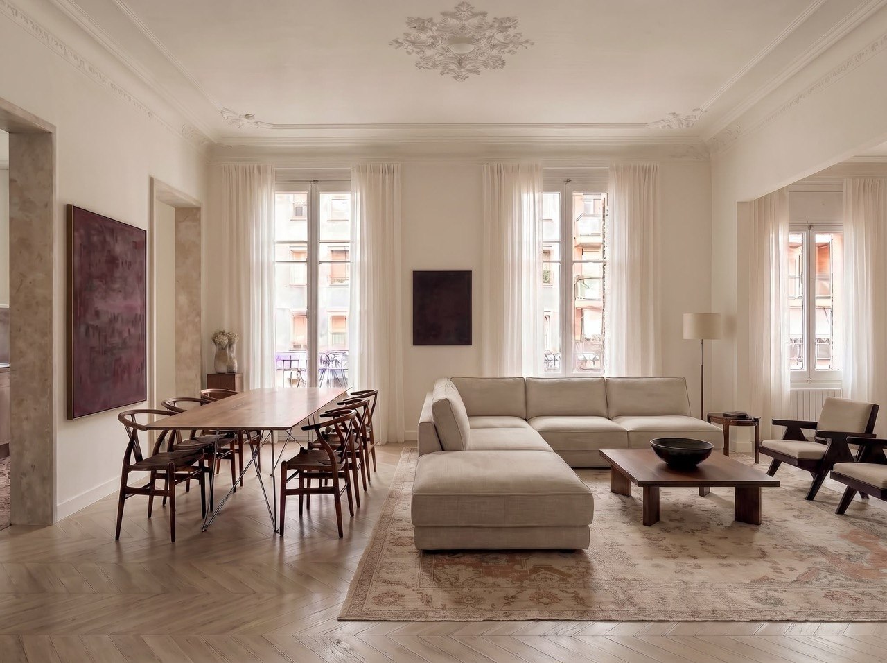 Salón con sofá esquinero, comedor al fondo y balcones con cortinas claras