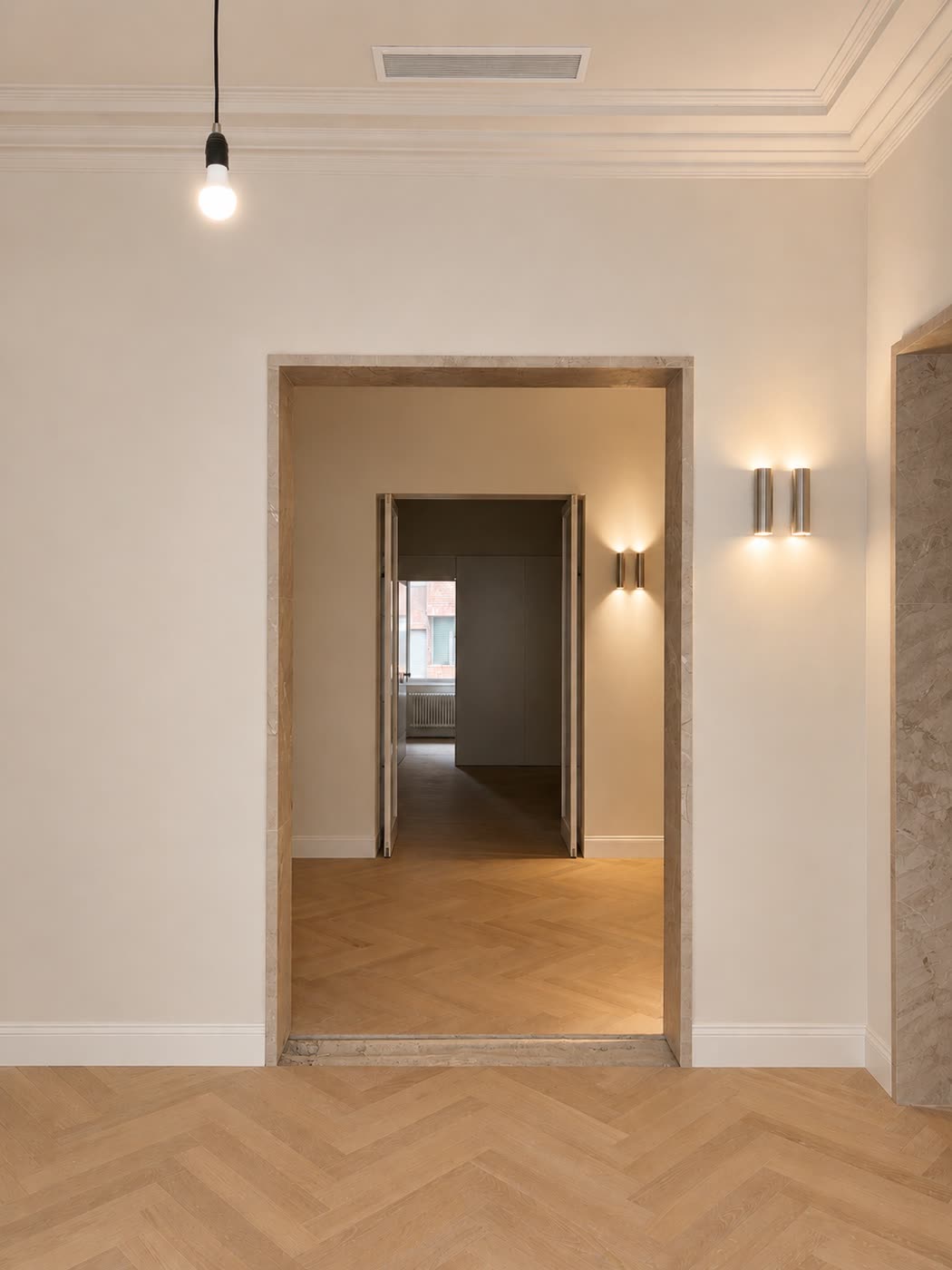 Paso entre estancias, con la puerta enmarcada en mármol, apliques de acero y el parquet de roble en espiga